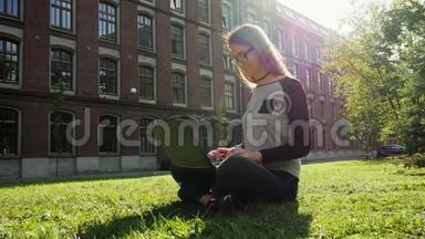 美丽而现代的女学生或自由职业者在笔记本电脑上工作，坐在校园绿色草坪上的公园里